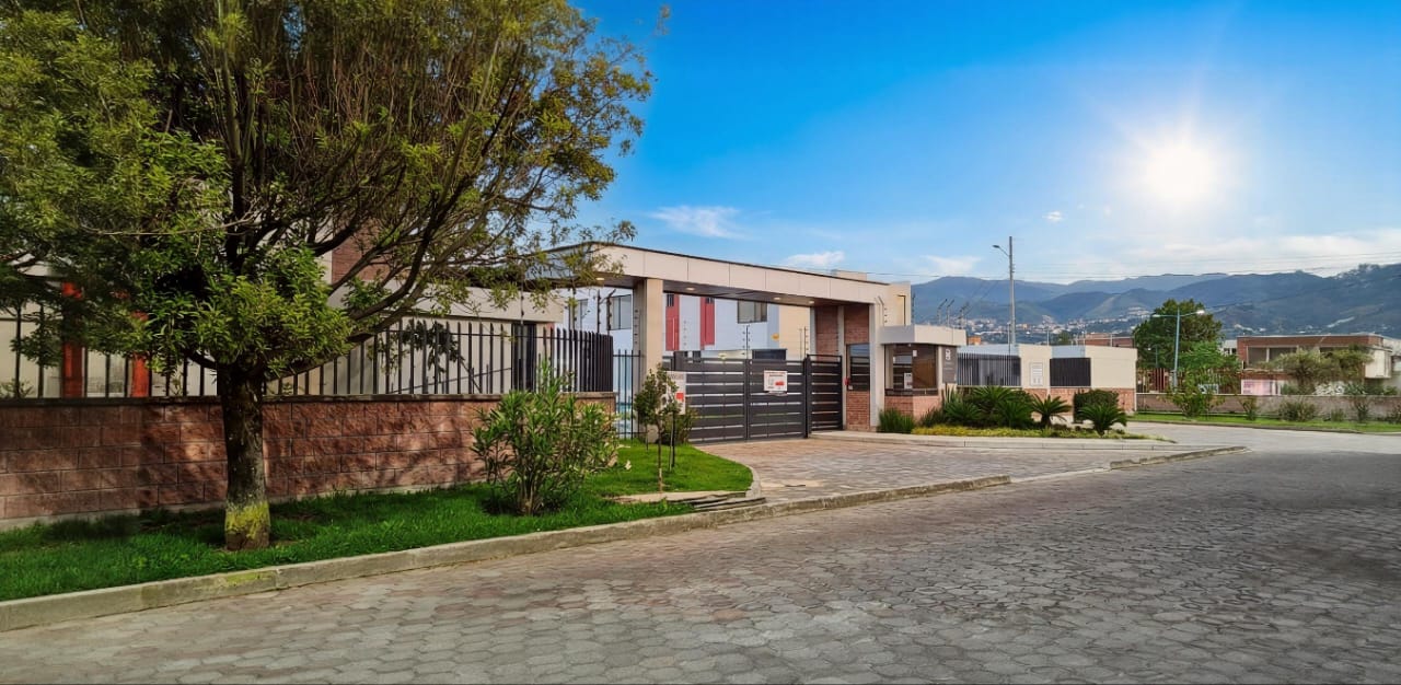 Calle adoquinada que entra al conjunto con un portón y casas bajas, sol y montañas al fondo, El Dean