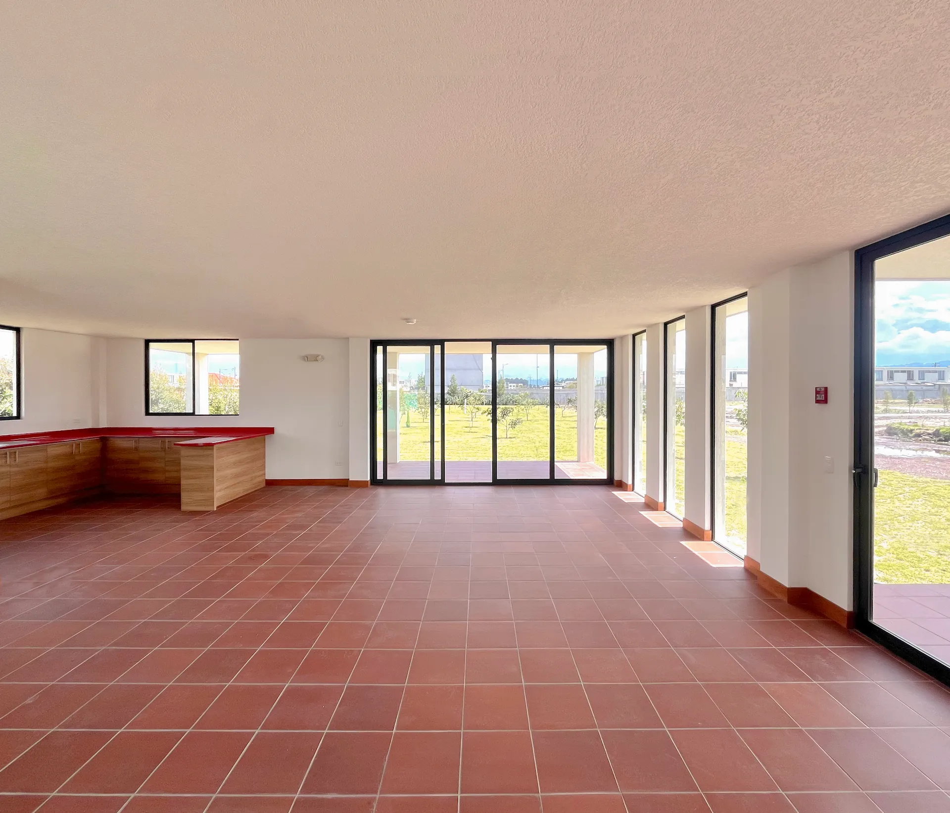 Sala comunal vacía con piso de baldosa roja y ventanales hacia el verde, Santa Lucía