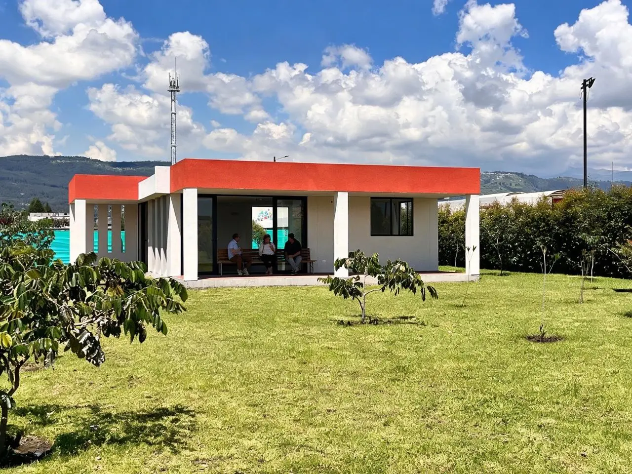 Sala comunal de una planta con techo teja sobre césped y nubes, Santa Lucía