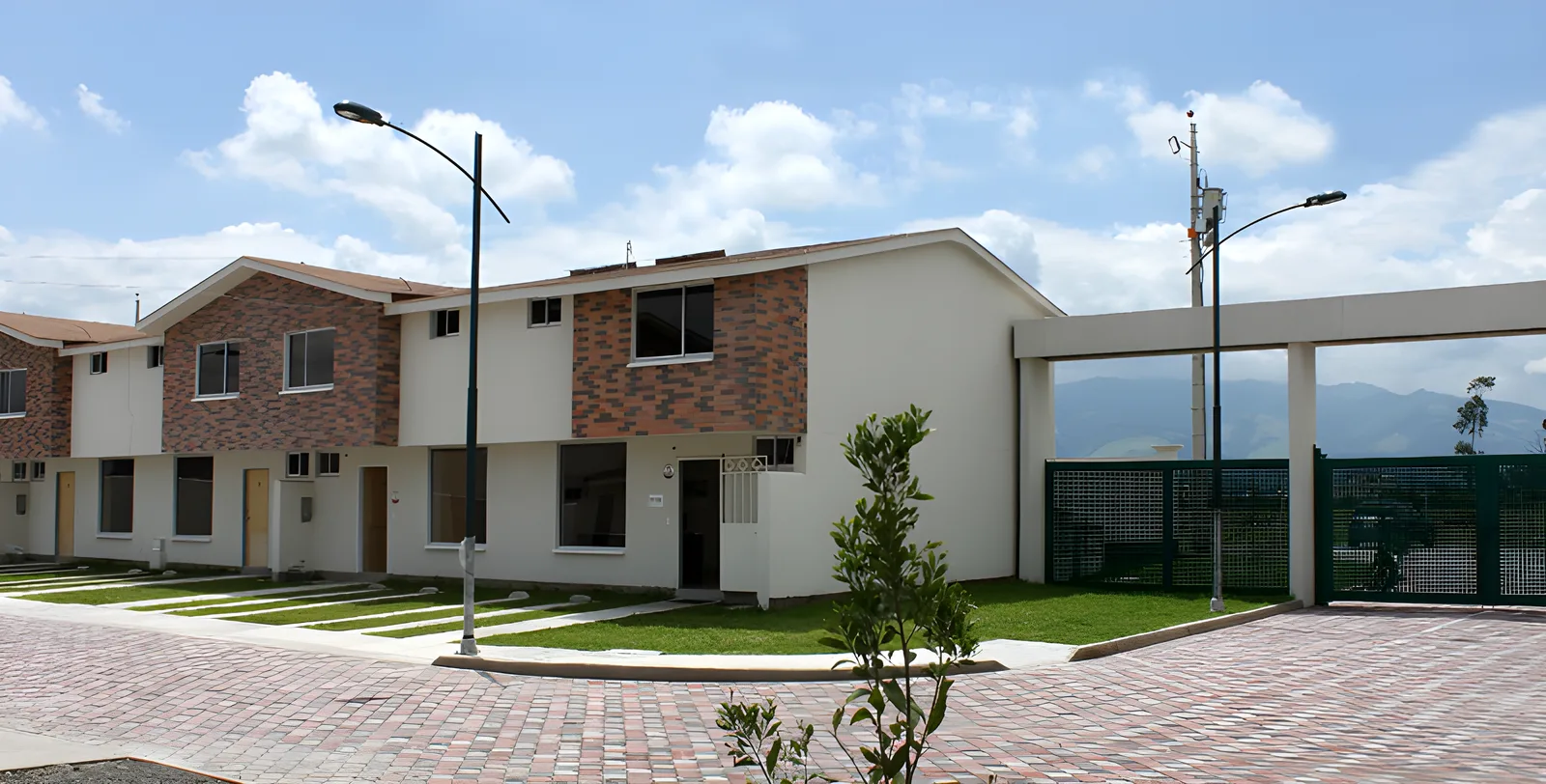 Casas blancas con ladrillo visto y portón de vidrio verde bajo cielo con nubes, Puerta del Sol El Dean