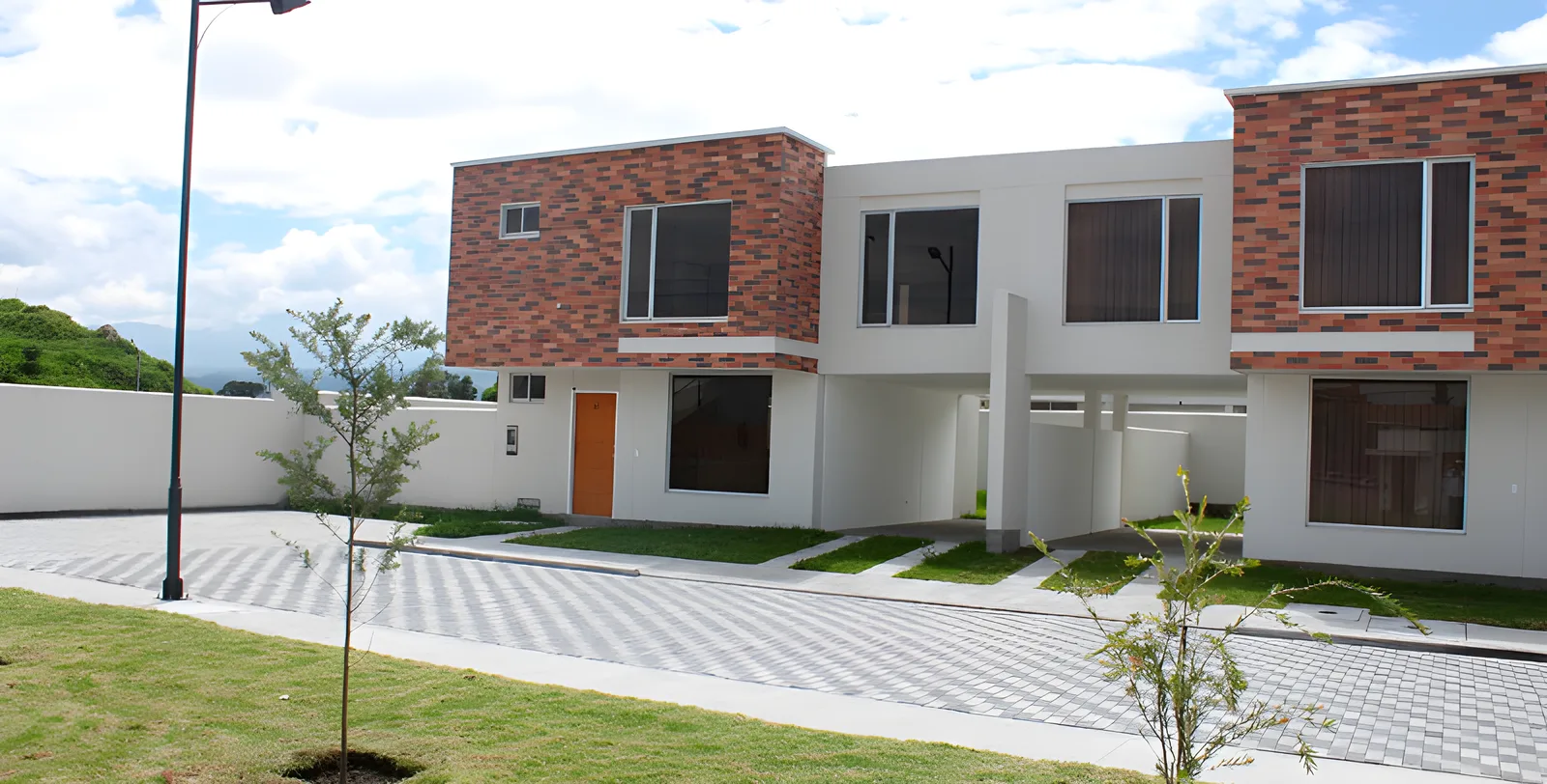 Casas blancas con ladrillo visto y puertas naranjas frente a un césped, Portal del Deán