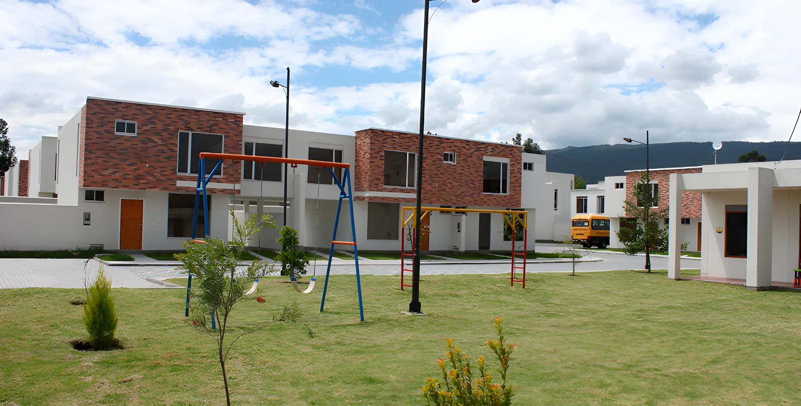 Parque con columpios y casas blancas detrás bajo cielo nublado, Portal del Deán