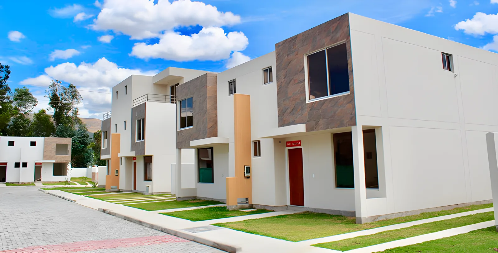 Esquina de casas blancas con revestimiento de piedra y puertas rojas bajo cielo azul con nubes, Jardines del Dean 2