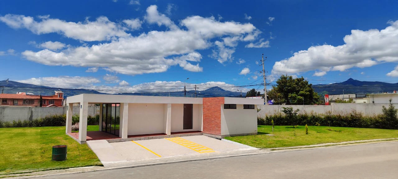 Sala comunal de una planta con jardín y el volcán al fondo bajo cielo con nubes, El Dean