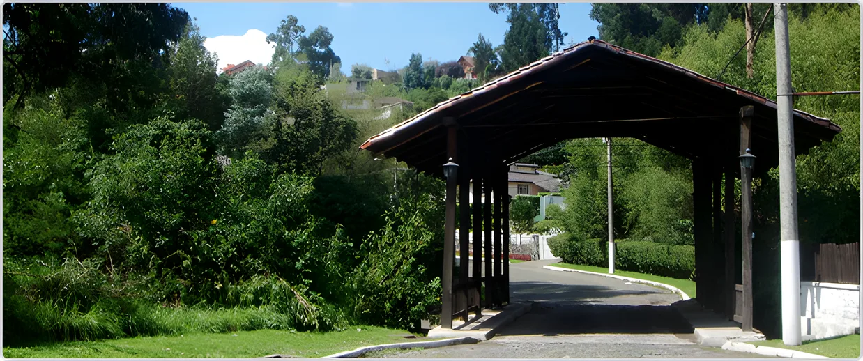 Pórtico de madera con techo de teja sobre el camino entre árboles, Portal de Los Chillos 1