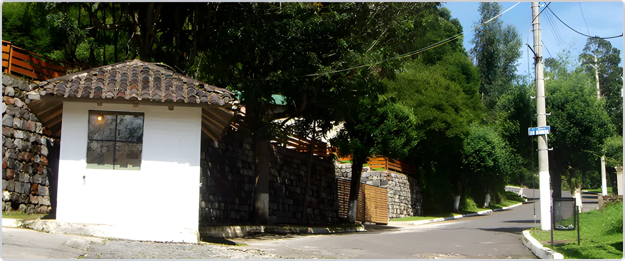 Casilla de entrada de piedra con techo de teja en una esquina arbolada, Portal de Los Chillos 2