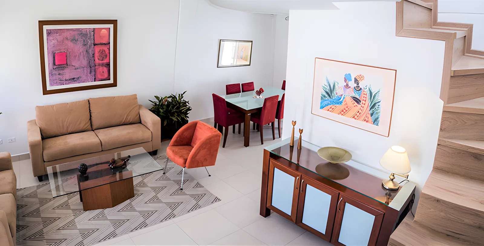 Sala con sofá café, sillón rojo y escalera de madera, casa modelo Jardines del Dean